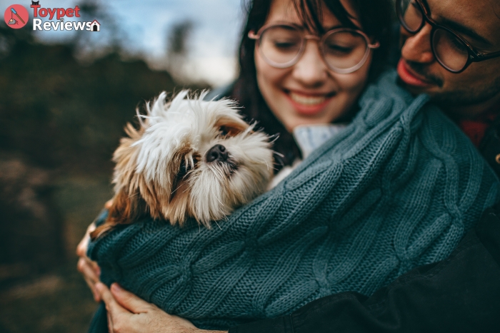two dog lovers cuddling a small dog in a blanket